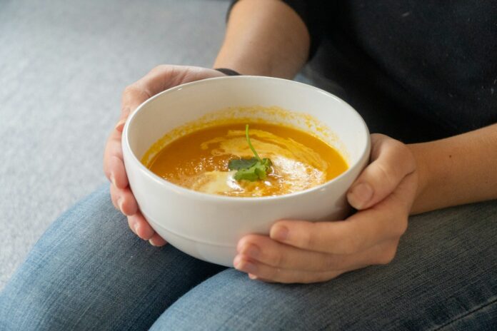 Person holding a bowl of creamy pumpkin soup