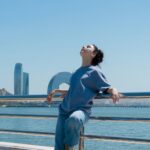 “깊은 잠이 주는 힘, 내 일상에 스며드는 건강 수면 루틴” Woman enjoys the sun with water and city views.